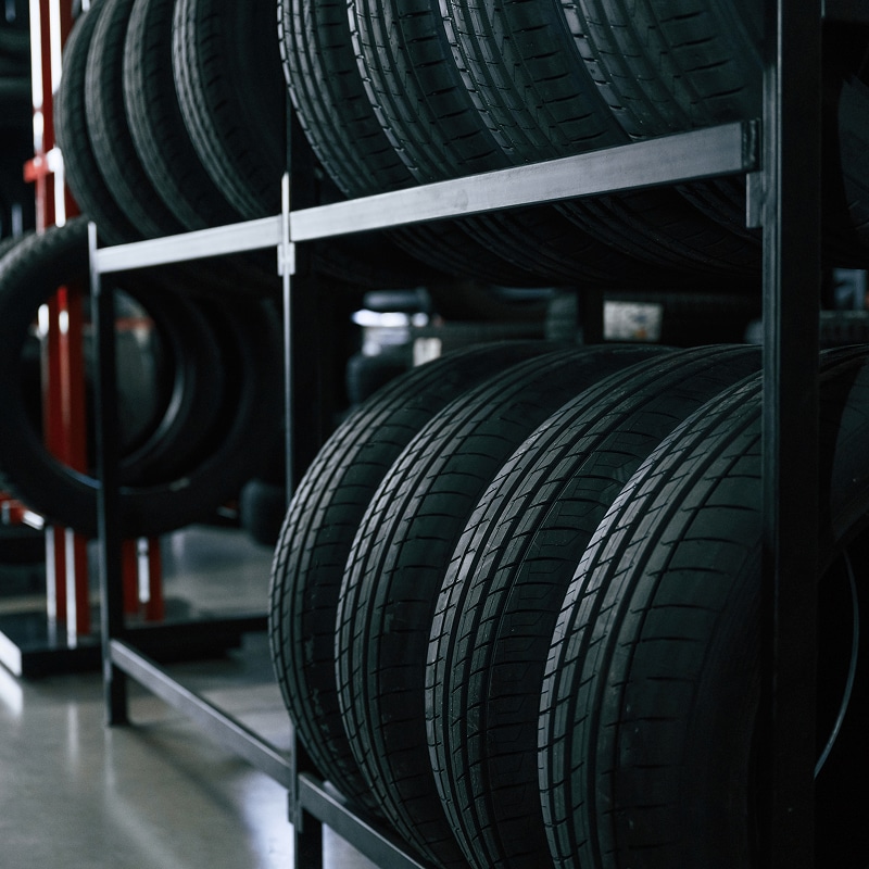 Pneus neufs stockés sur deux étagères métalliques noires dans un garage automobile. Le rayonnage contient plusieurs rangées de bandes de roulement.