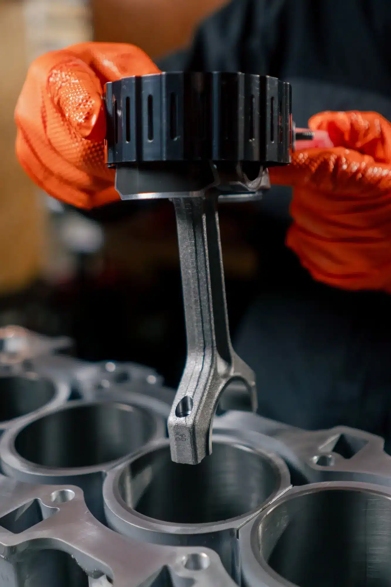 Assemblage moteur : un technicien en gants orange guide une bielle et son compresseur de segments dans un cylindre du bloc.