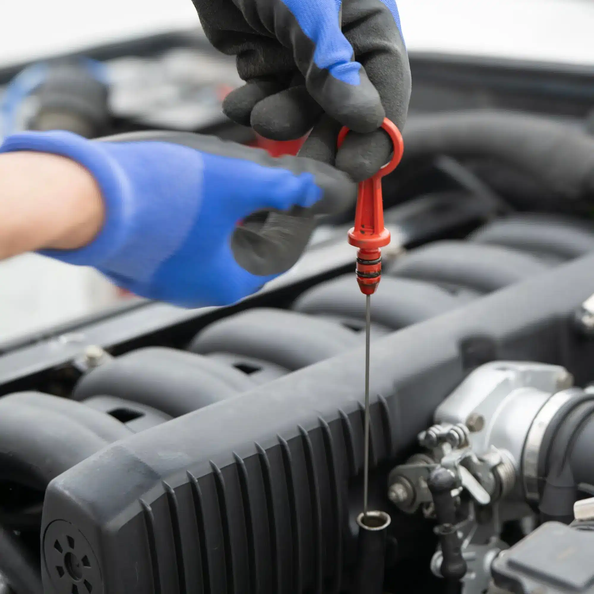 Main gantée vérifiant le niveau d'huile du moteur en retirant la jauge rouge. Entretien essentiel de mécanique automobile.