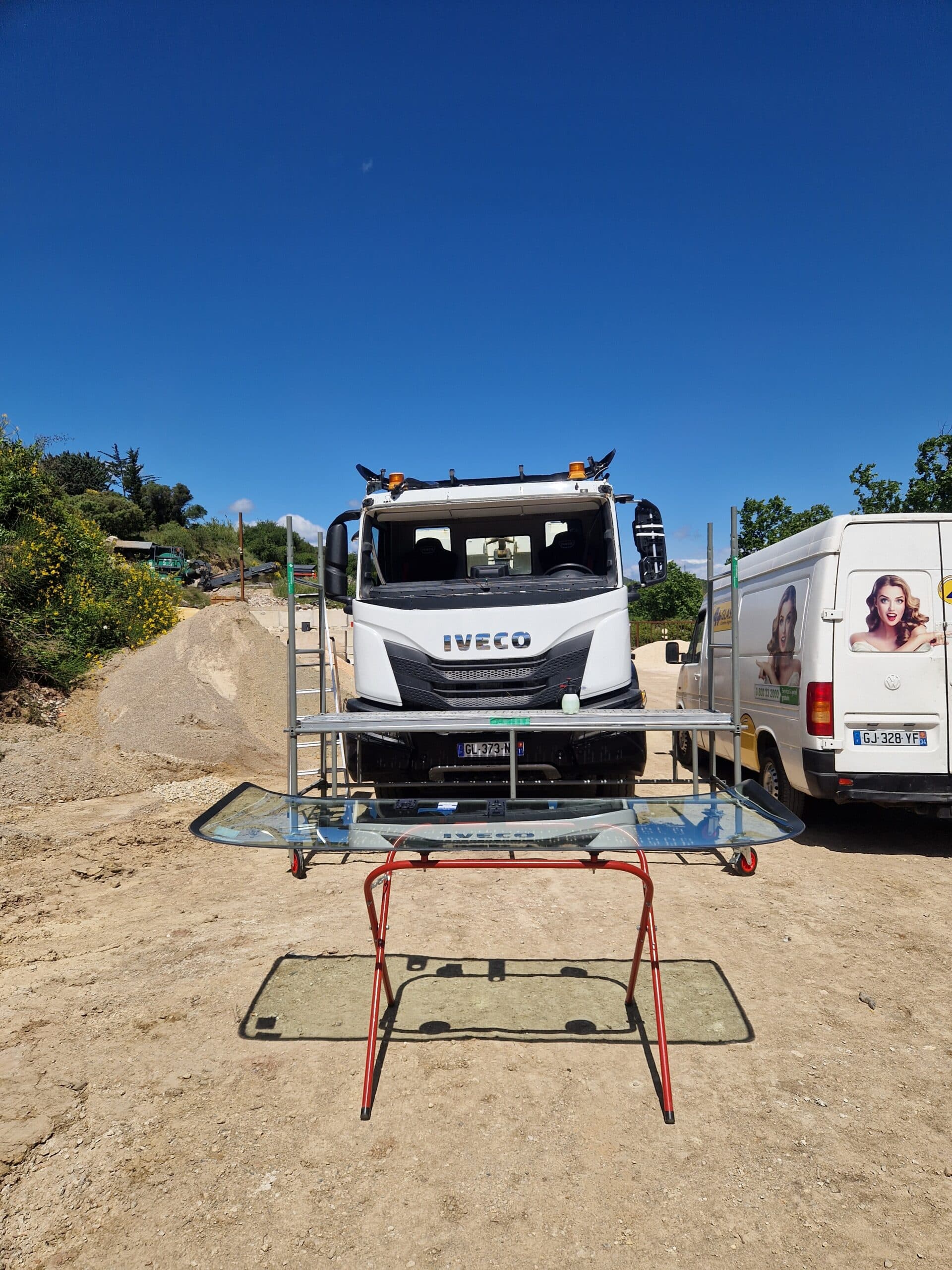 Installation de pare-brise sur camion Iveco blanc avec support mobile et fourgon A Glass sur un chantier.