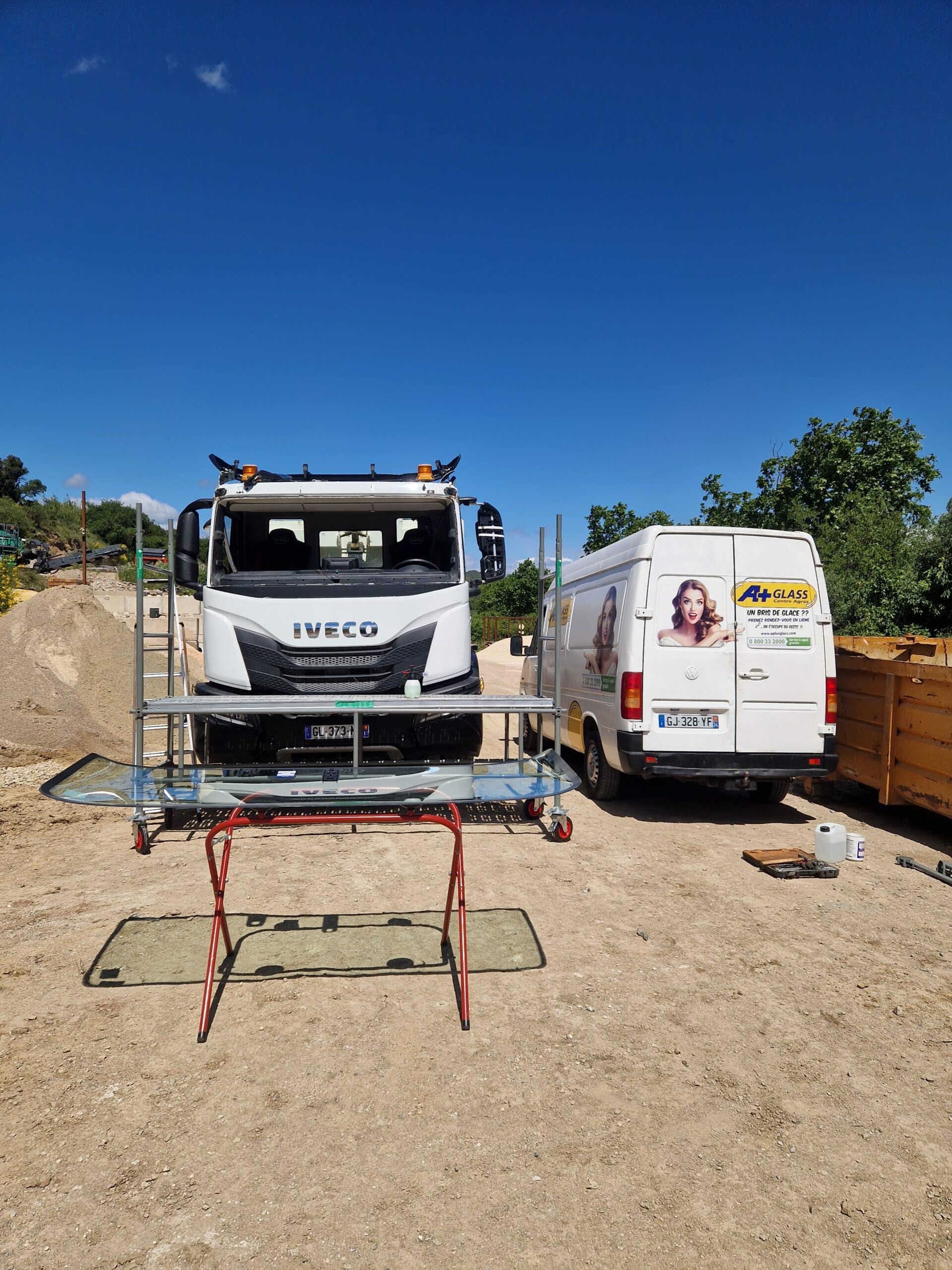 Technicien A+ Glass remplaçant le pare-brise d'un camion Iveco sur un chantier. Texte : Un bris de glace ??.
