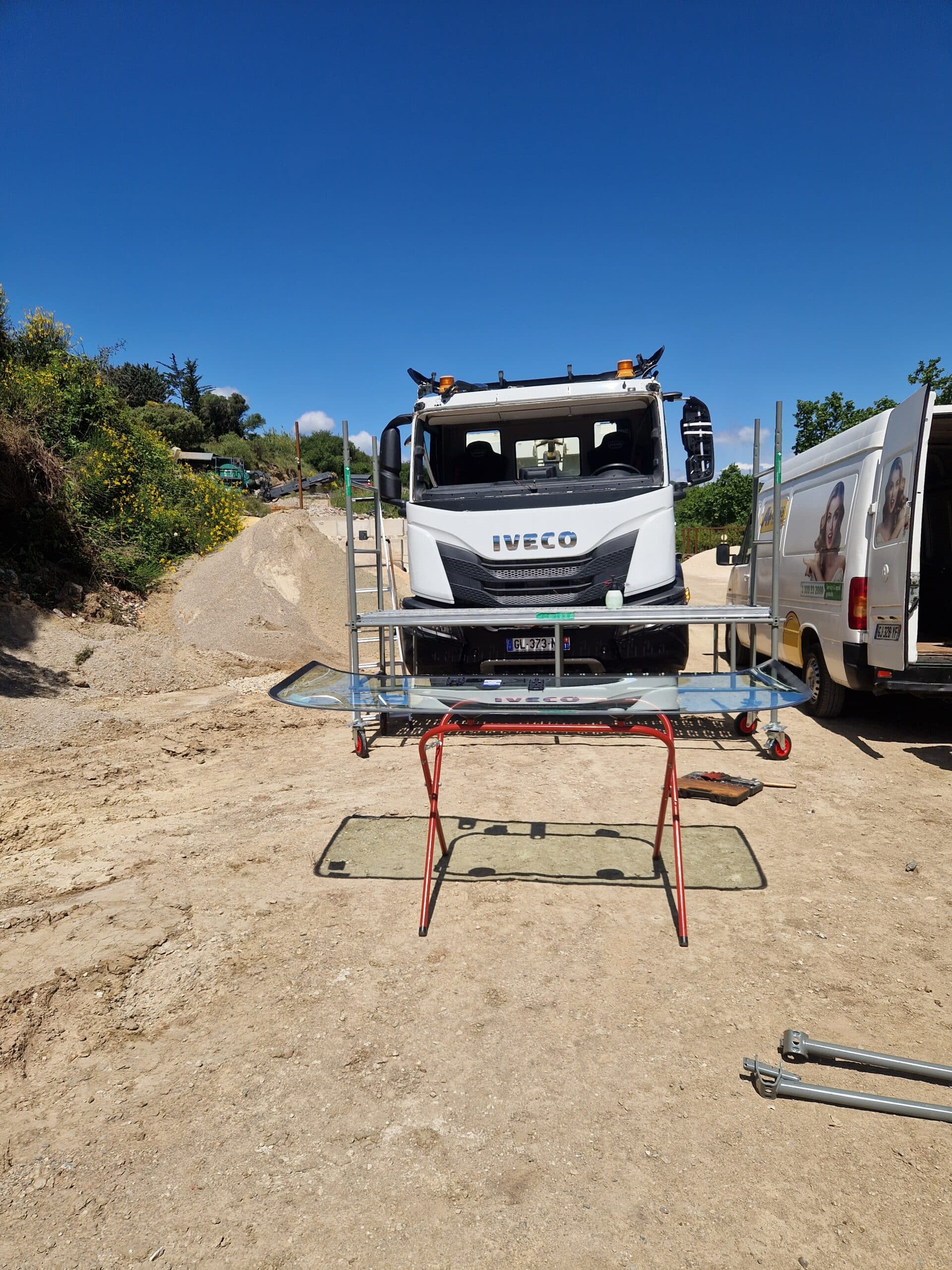 Nouveau pare-brise sur stand devant un camion Iveco blanc pour un remplacement mobile sur chantier.